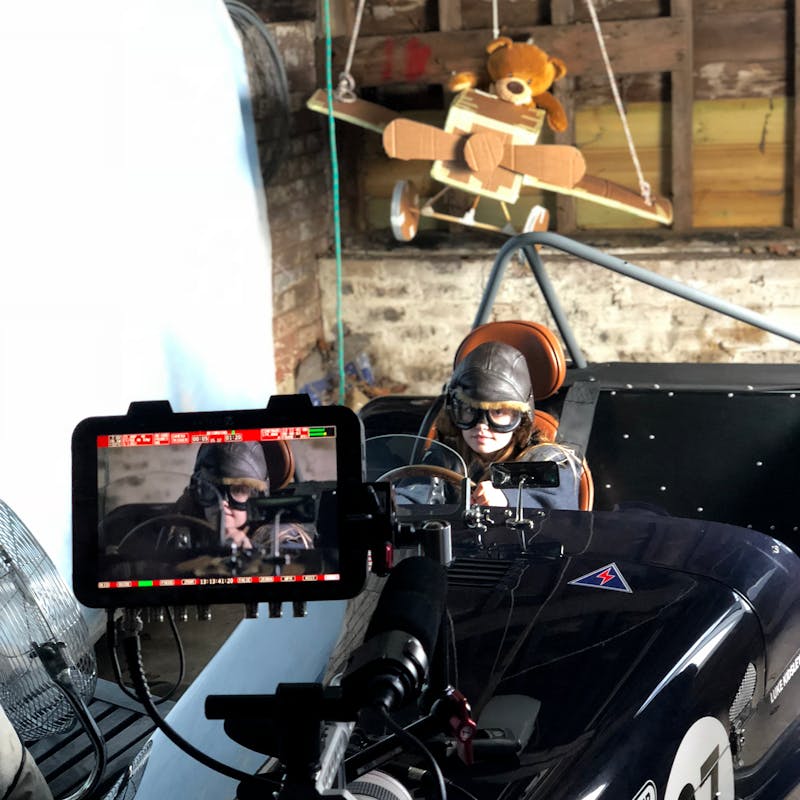 Behind the scenes filming a young girl playing in a Caterham Car with her teddy behind her