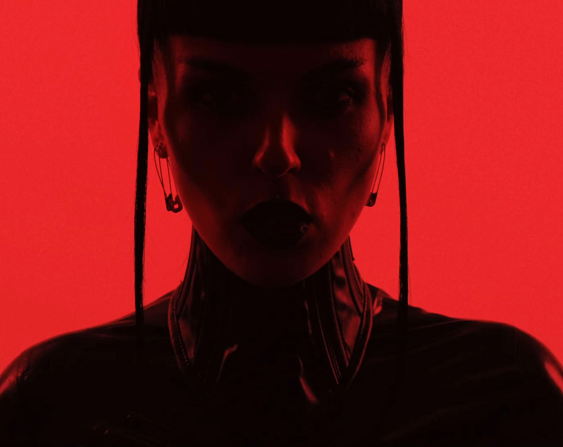 Close-up silhouette of a person wearing safety pin earrings on a red background