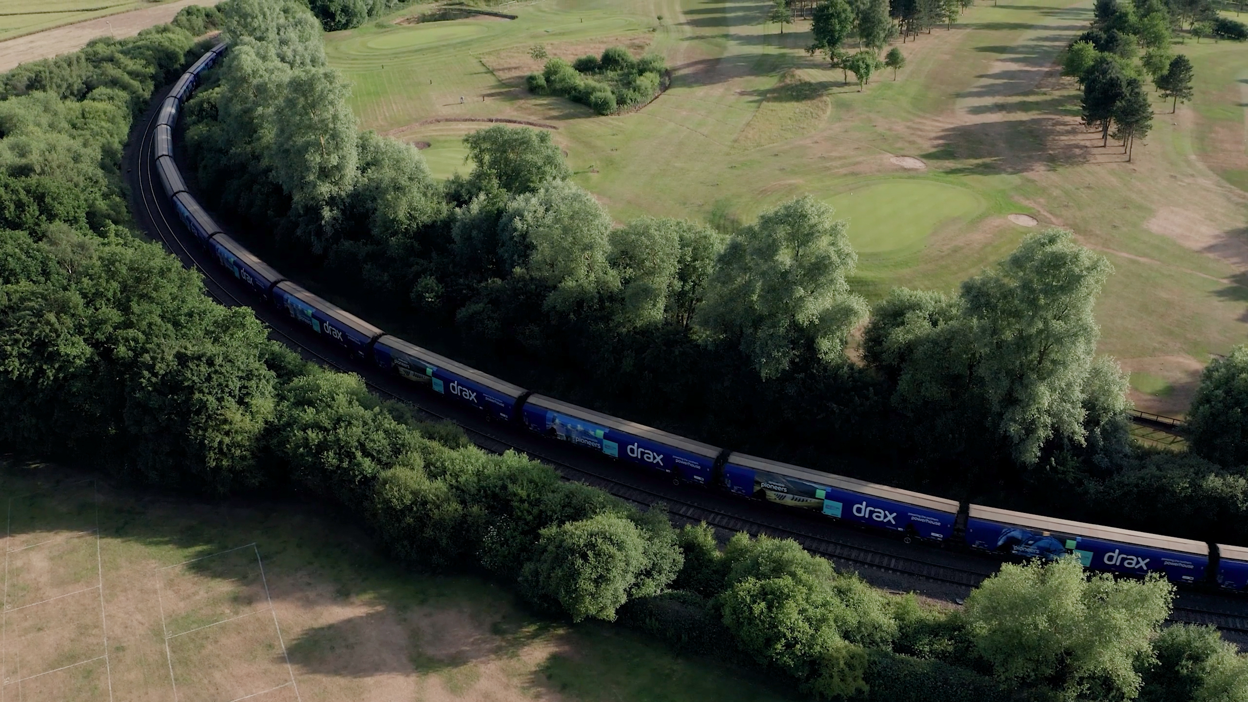 Aerial photography of a Drax branded train passing through tree lined train tracks 