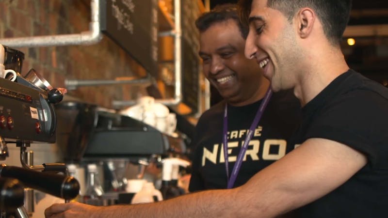 Two Caffè Nero employees smiling whilst making coffee