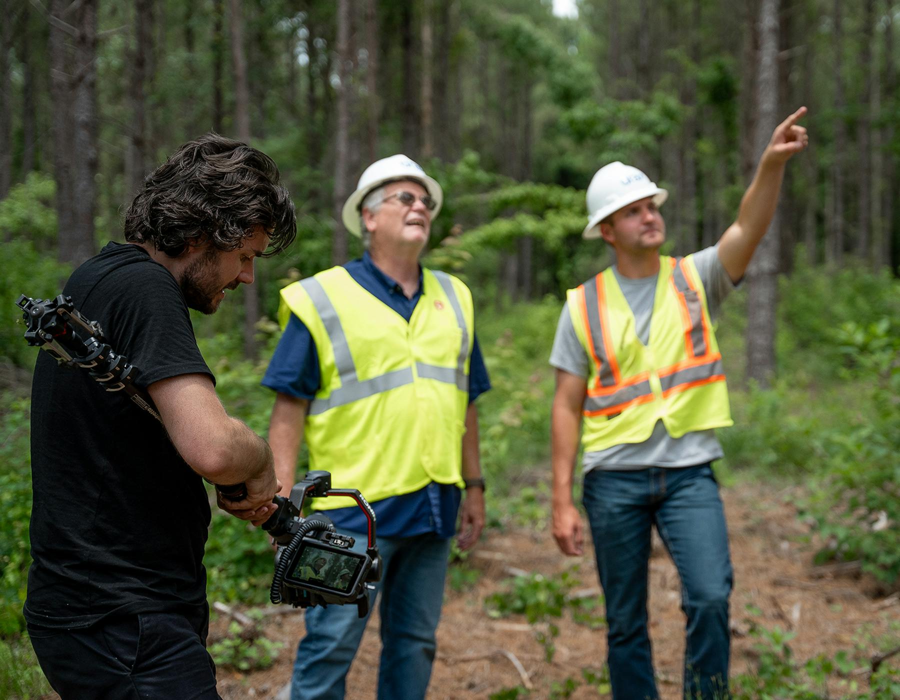 Behind the scenes image of a camera man capturing two engineers pointing at trees