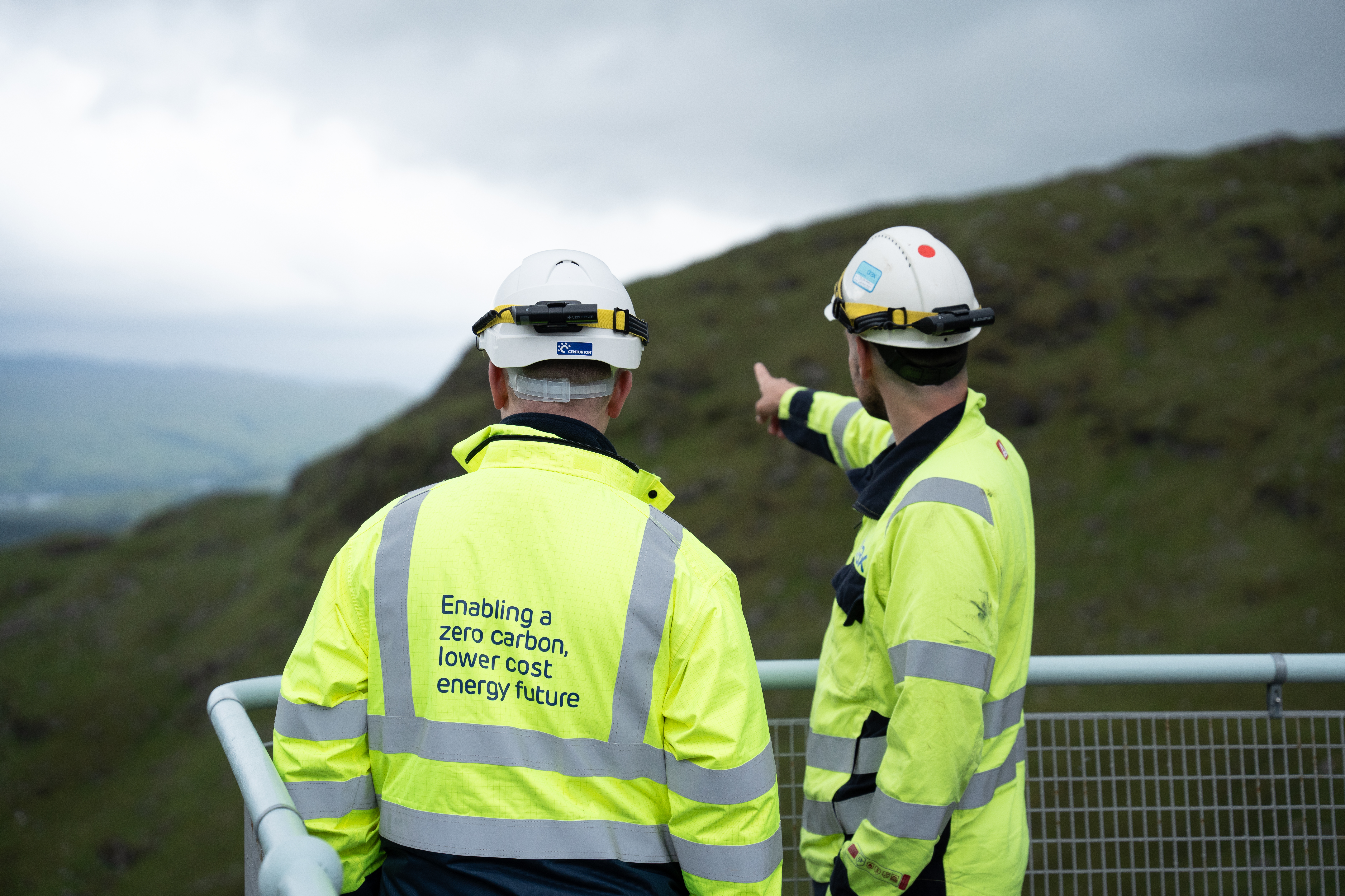 two engineers atop a dam, looking out and pointing into the distance