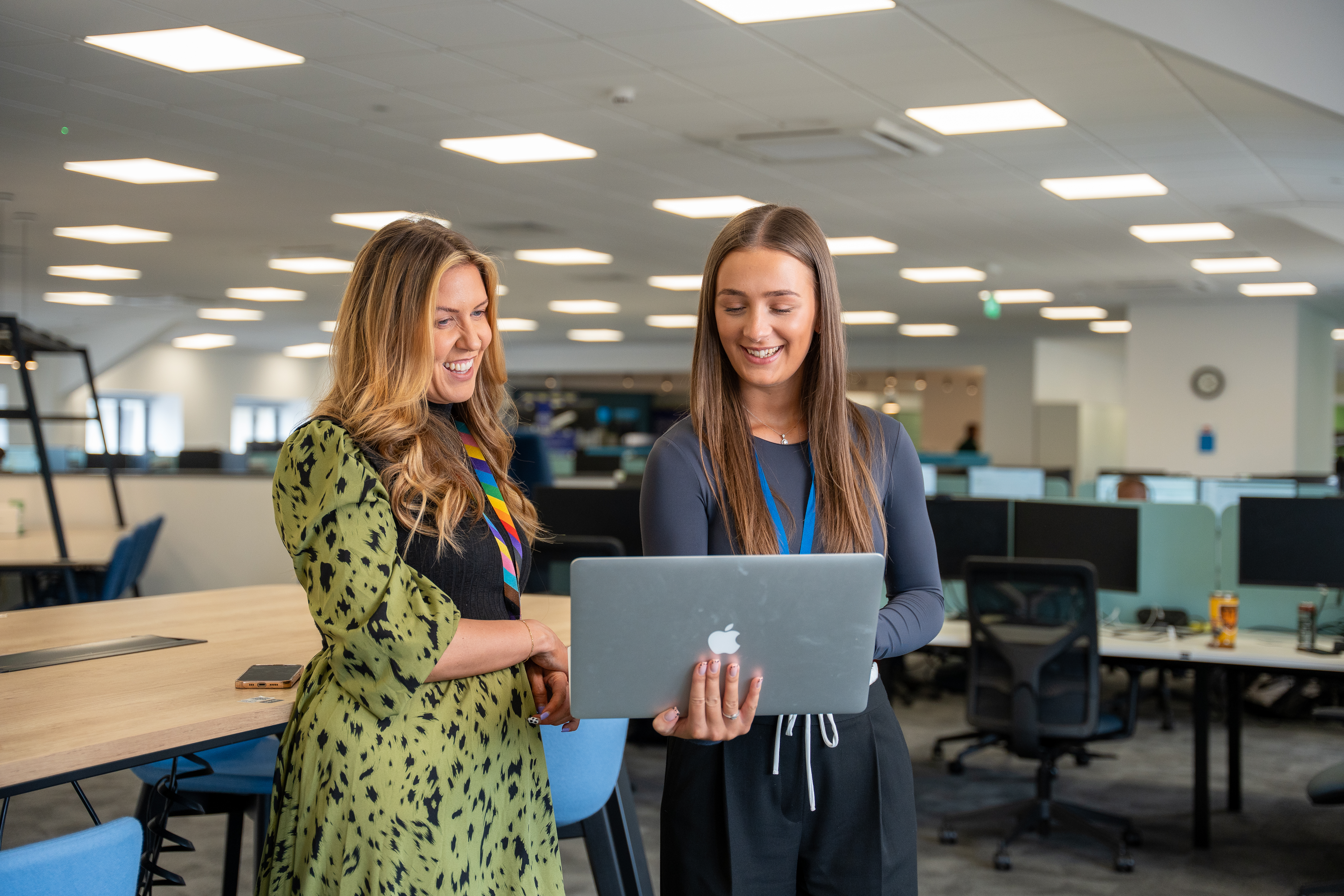 two female colleagues in an office smiling and looking at a laptop 