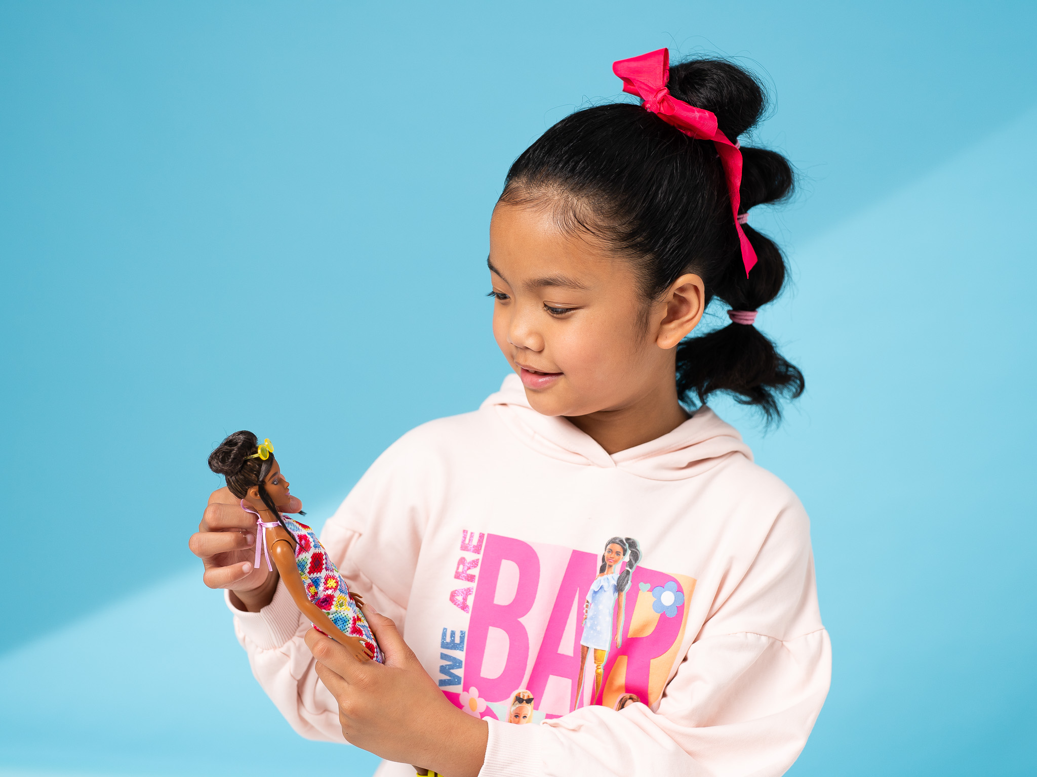 young girl in a barbie hoody holds and looks down at her barbie doll