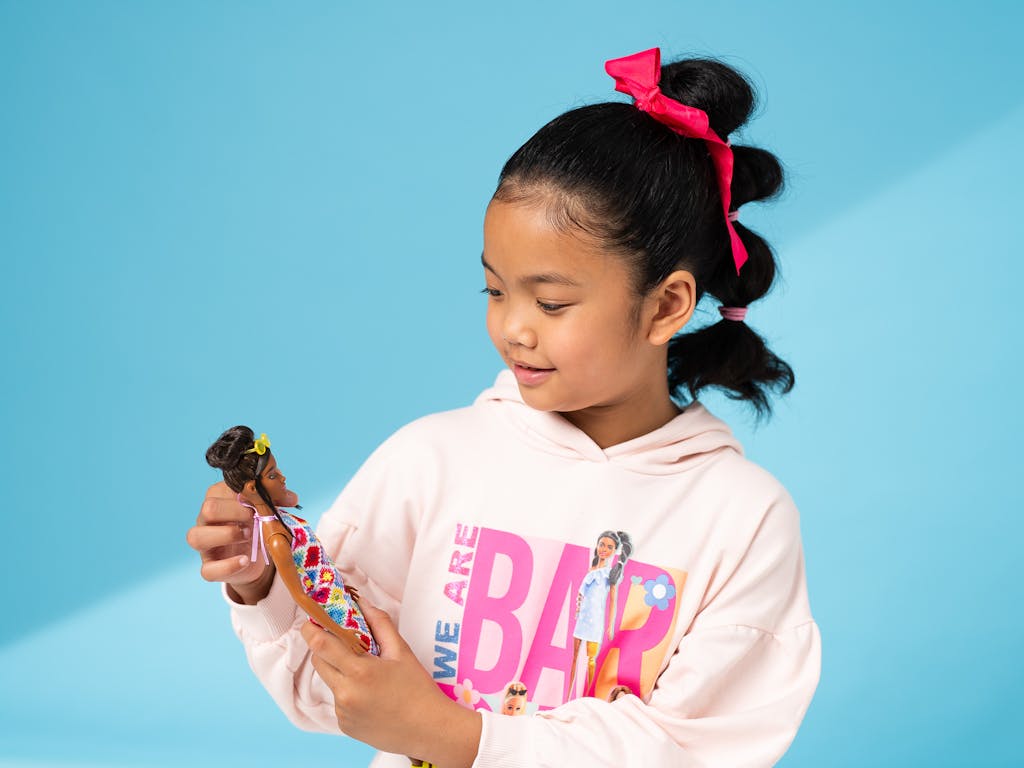 young girl in a barbie hoody holds and looks down at her barbie doll