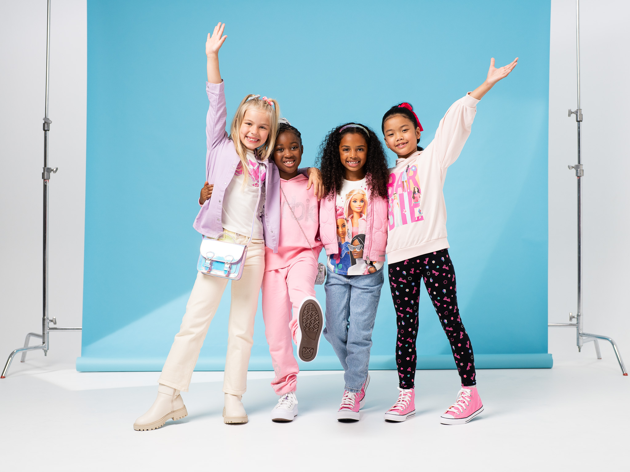 4 girls dressed in fashionable barbie clothes, posing together, hands in the air