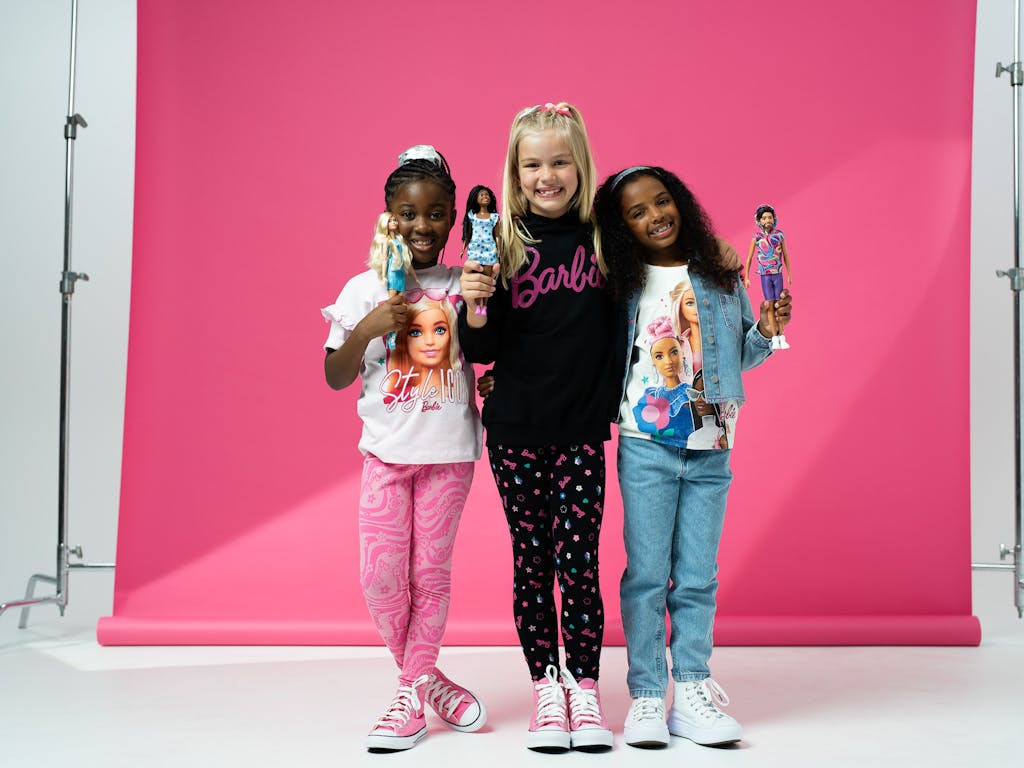 3 girls dressed in Barbie clothing, holding barbie dolls, smiling for the camera