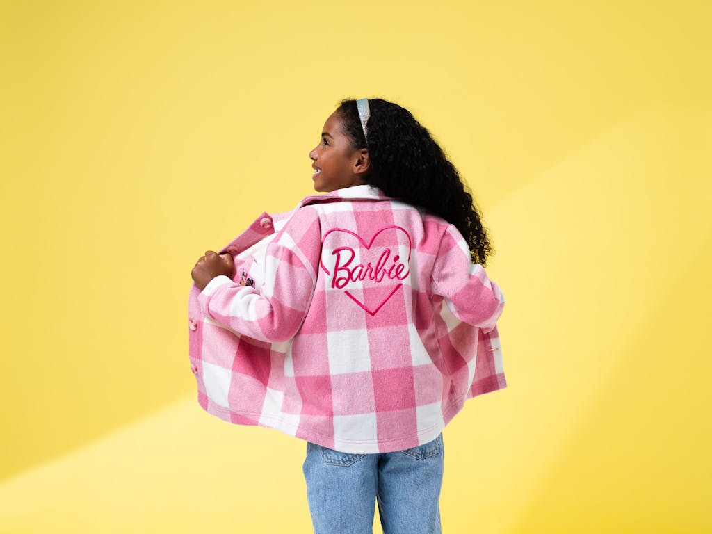child poses, with back to camera, wearing a barbie fleece shacket