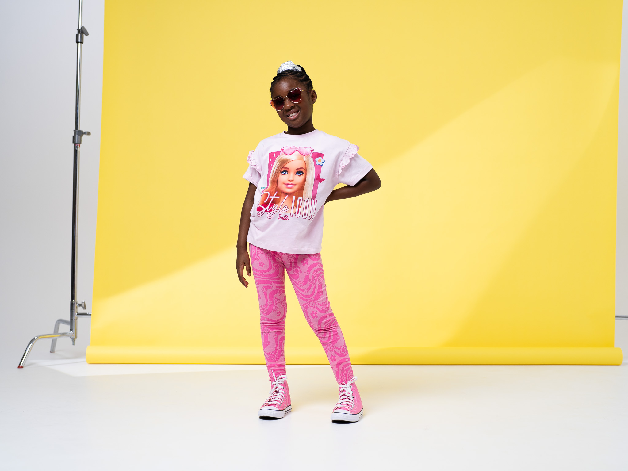 child poses hand on hip, wearing a barbie tshirt and leggings with pink sunglasses