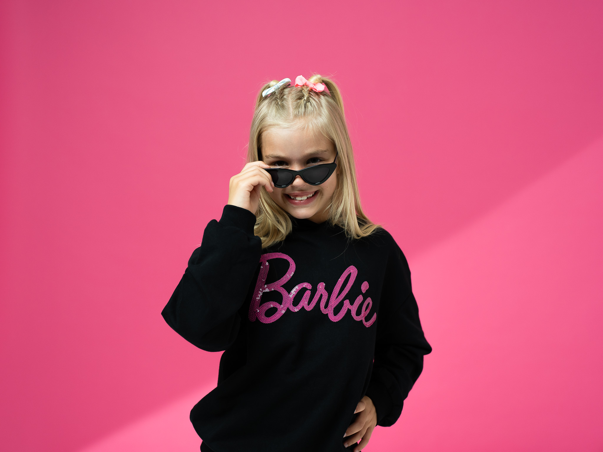 Young girl in black and pink barbie hoody and black sunglasses, poses and smiles to the camera