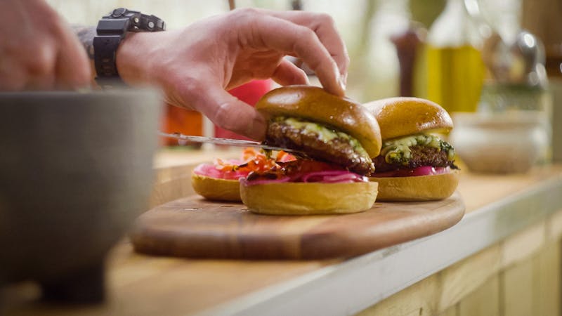 hand plating fresh burgers onto brioche buns dressed with pink pickles