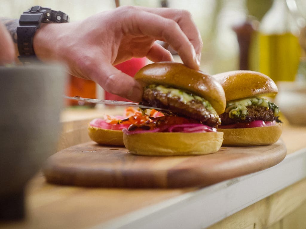 hand plating fresh burgers onto brioche buns dressed with pink pickles