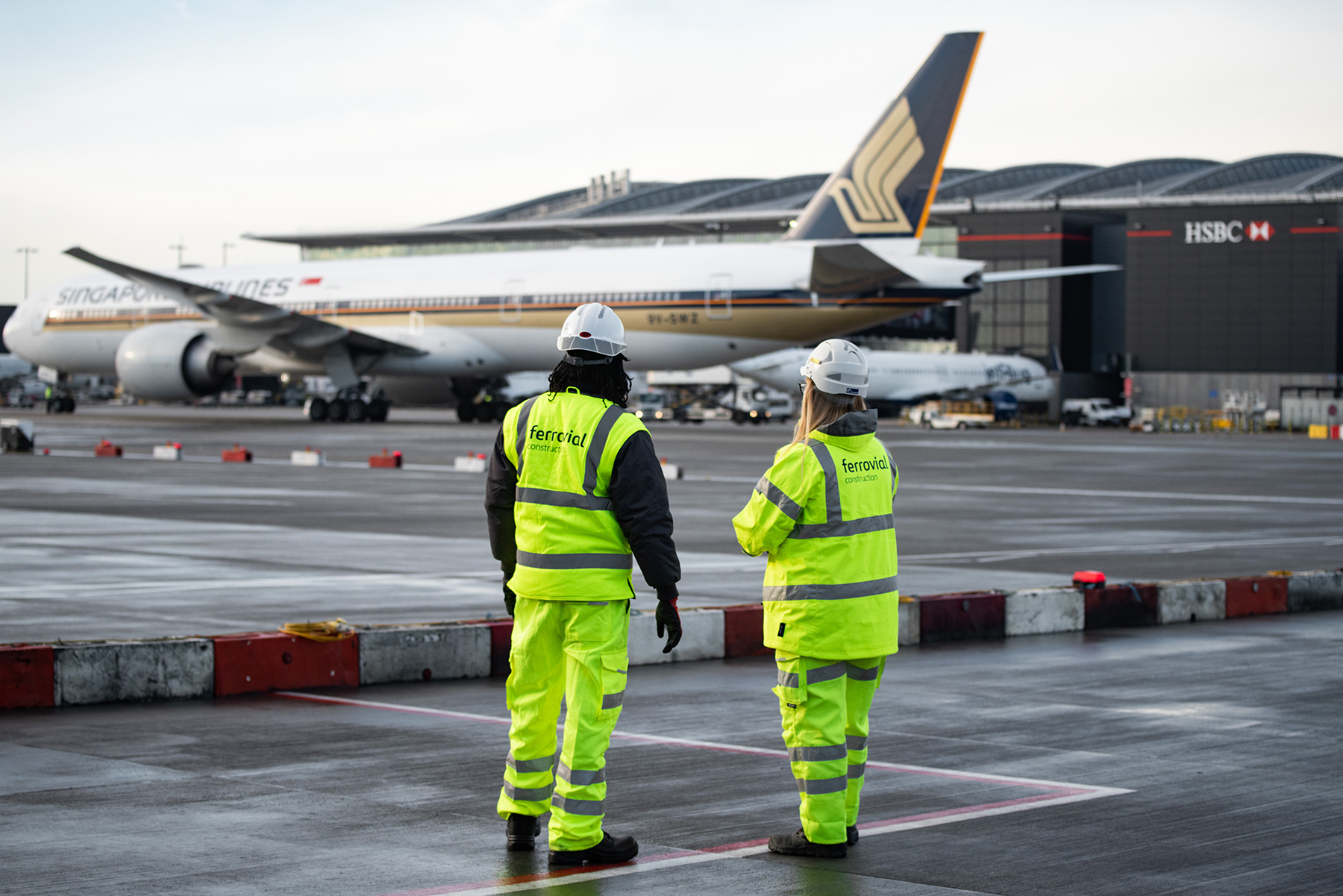 Two engineers dressed in high-vis watching a plane take off