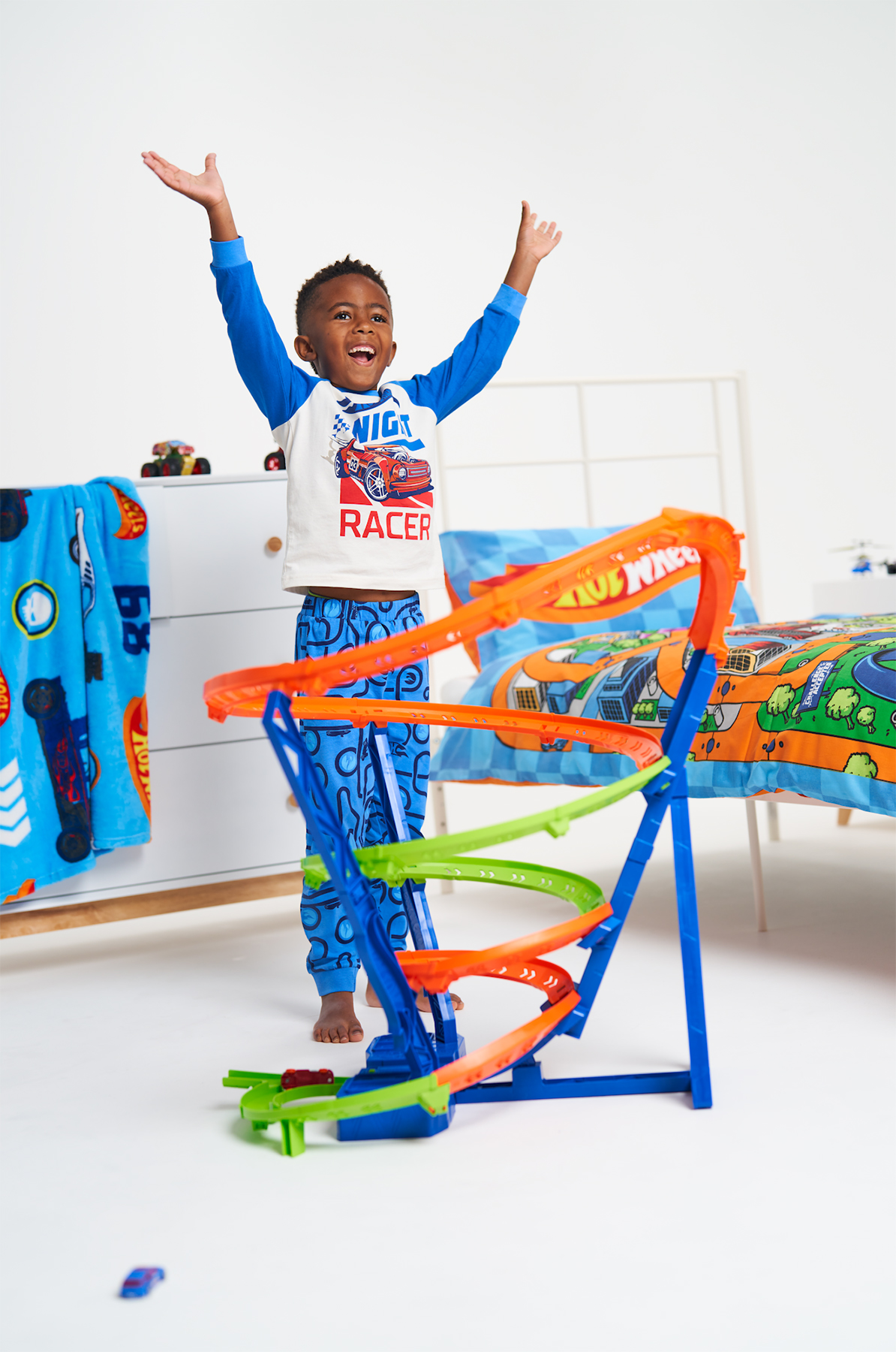 Young boy playing with a Hot Wheels race track, cheers with his arms above his head