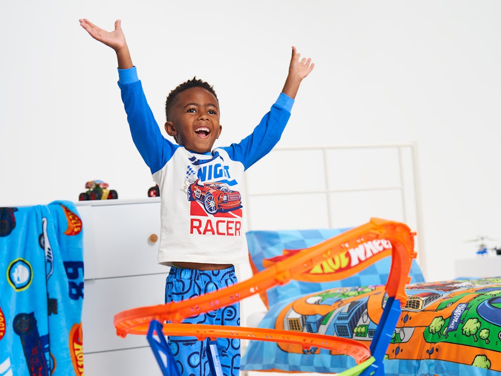 Young boy playing with a Hot Wheels race track, cheers with his arms above his head