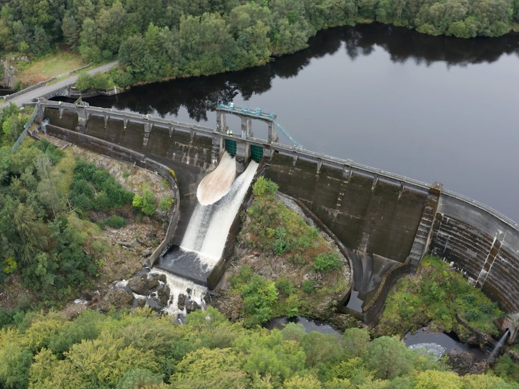 Aerial drone photo of water rushing through gates of a hydro-power damn in Scotland