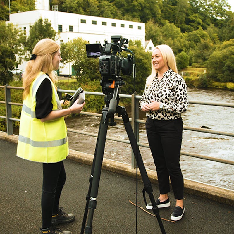 Director dressed in high-vis filming talking to a smiling corporate lady in front of a camera