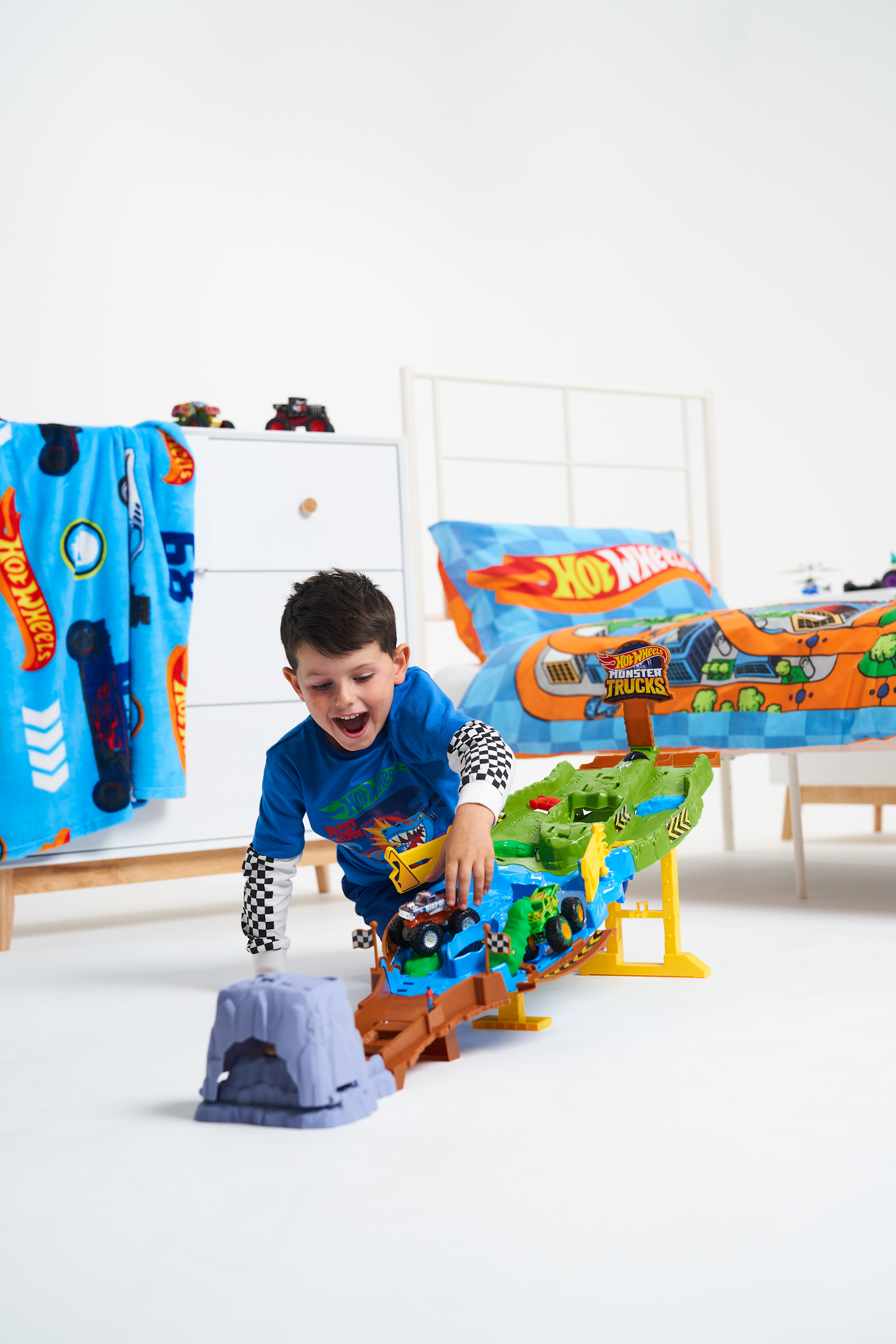 a young boy play with a Hot Wheels race track, in a child's bedroom
