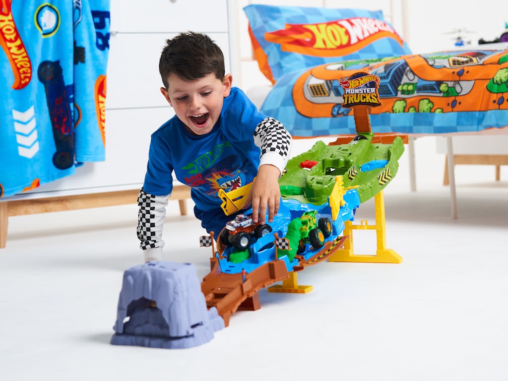 a young boy play with a Hot Wheels race track, in a child's bedroom