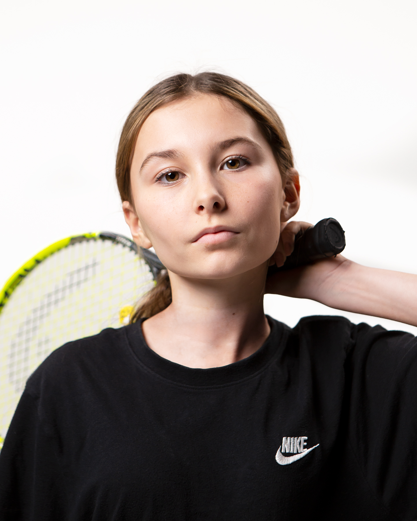 Teenage girl in Nike brand sports T shirt holds tennis racket behind her head