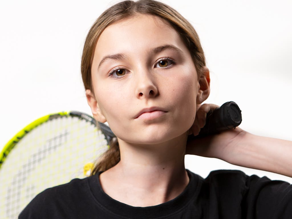 Teenage girl in Nike brand sports T shirt holds tennis racket behind her head