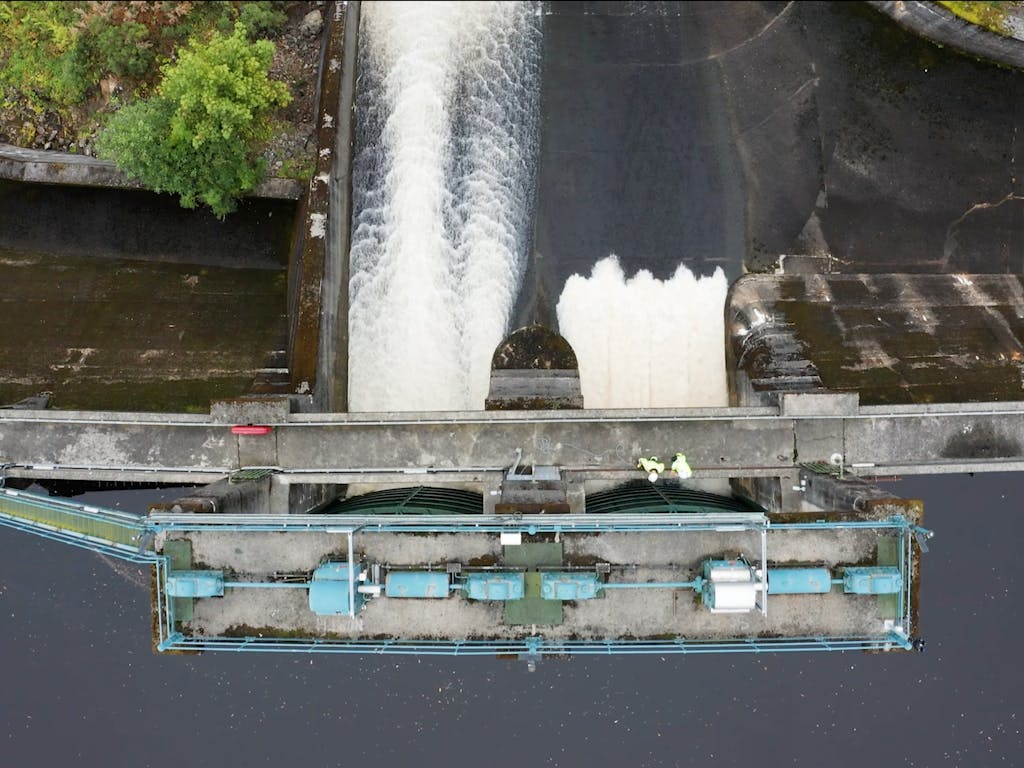 Aerial drone photo of water rushing through gates of a hydro-power damn in Scotland