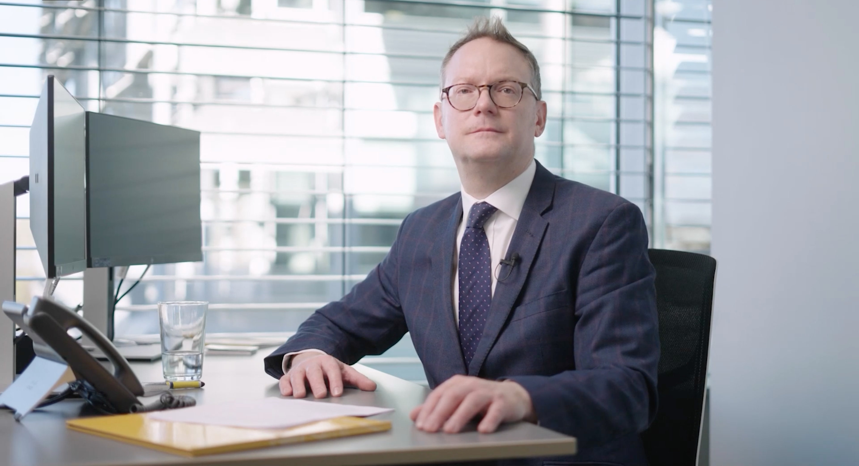 Corporate business man in suit sat at a computer desk in front of a glass window