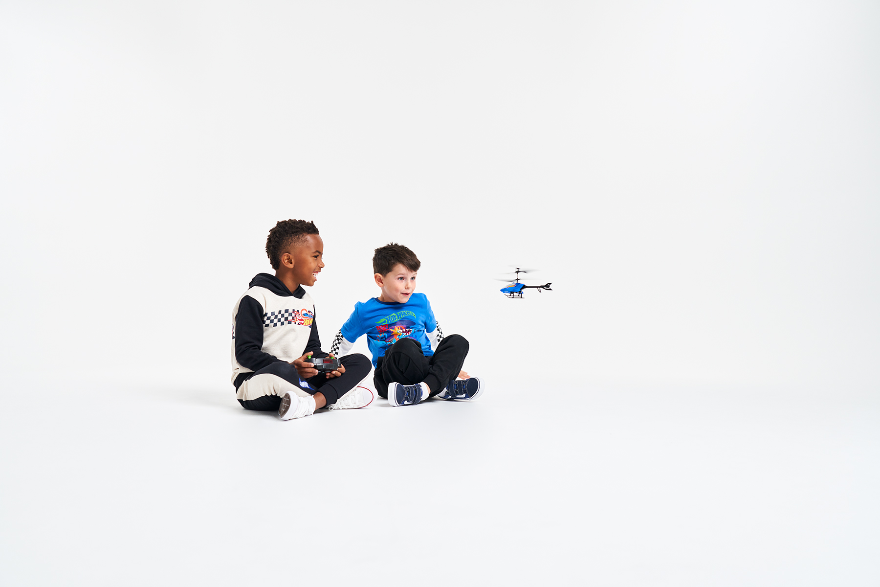 Two young boys smiling, playing with a Hot Wheels remote controlled helicopter