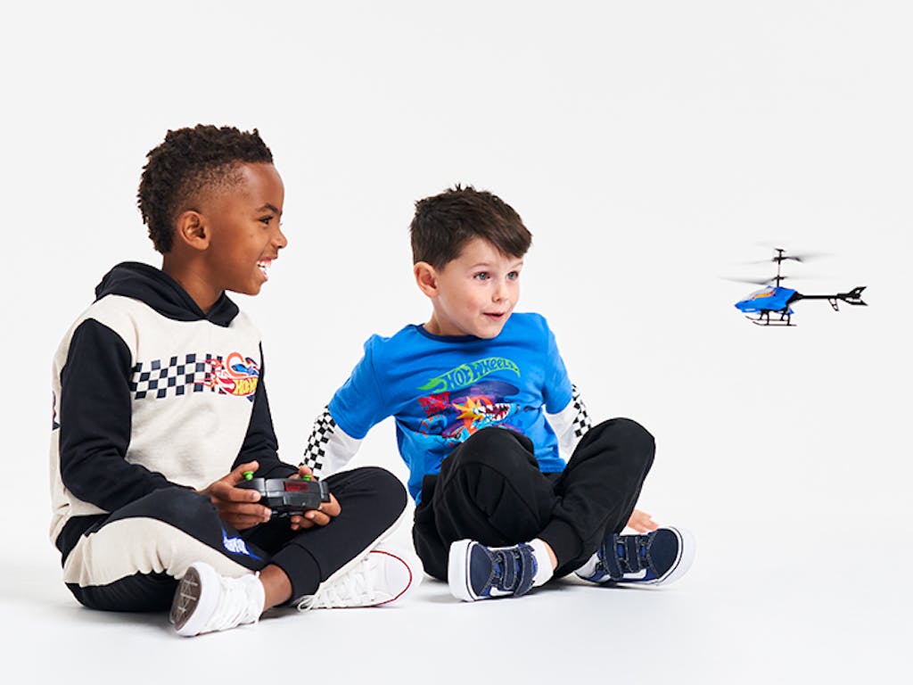Two young boys smiling, playing with a Hot Wheels remote controlled helicopter