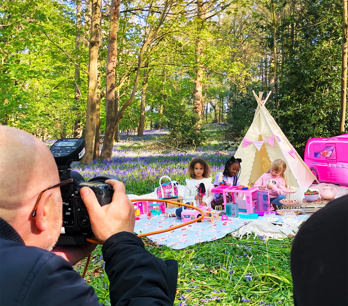 photographer takes picture of 3 young girls having a Barbie tea party in a bluebell covered woodland