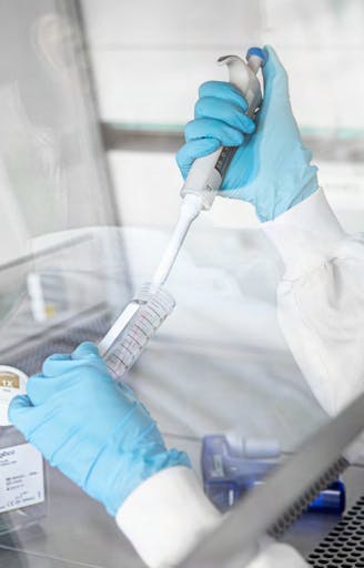 Laboratoriepersonal i sterila handskar använder en pipett för att hantera prover i ett säkerhetsklassat arbetsflöde, vilket illustrerar ChemoMetecs fokus på precisionsarbete och bioteknologiska lösningar.
