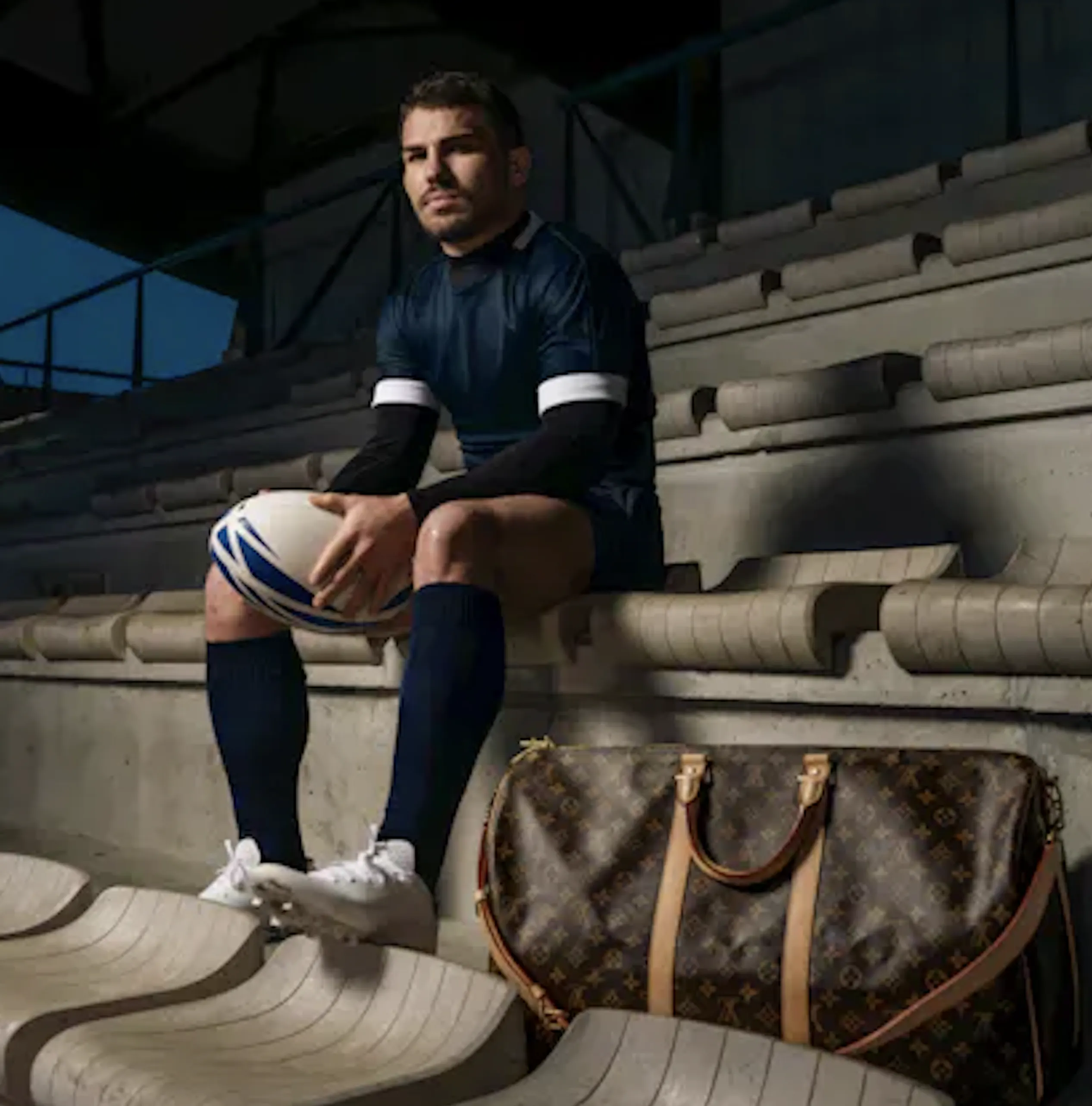 Antoine Dupont sitting in the bleachers holding a rugby ball 