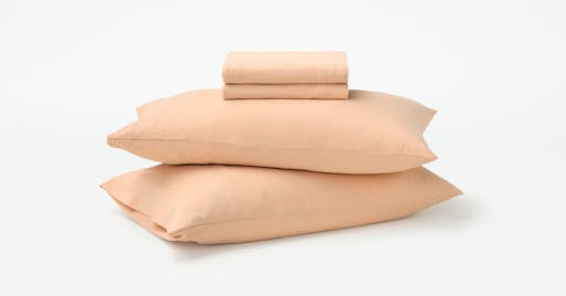Folded Organic Jersey Sheets on top of two pillows in Melon color. 