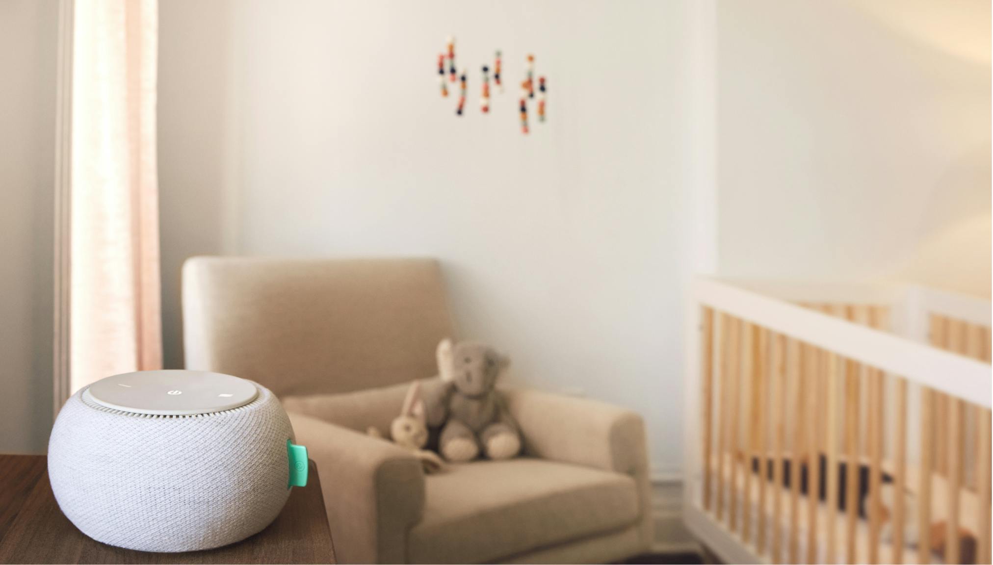 White Noise Machine in foreground of nursery with nursing chair and crib in background.