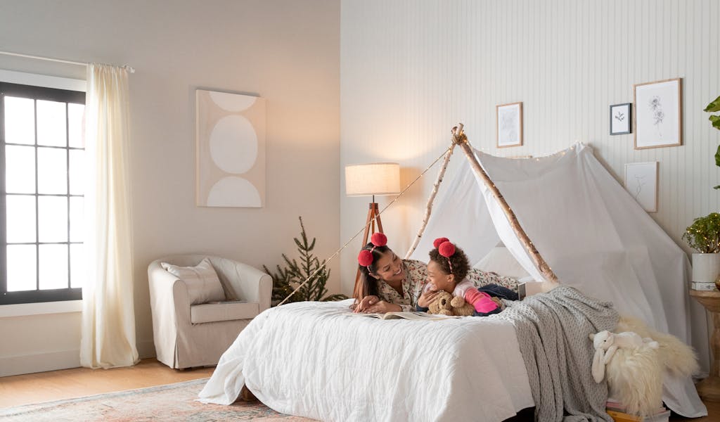 Mother and daughter playing and relaxing in fort built over a bed.