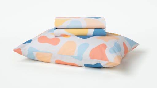 Our Palette patterned toddler sheet set folded sitting on top of a pillow