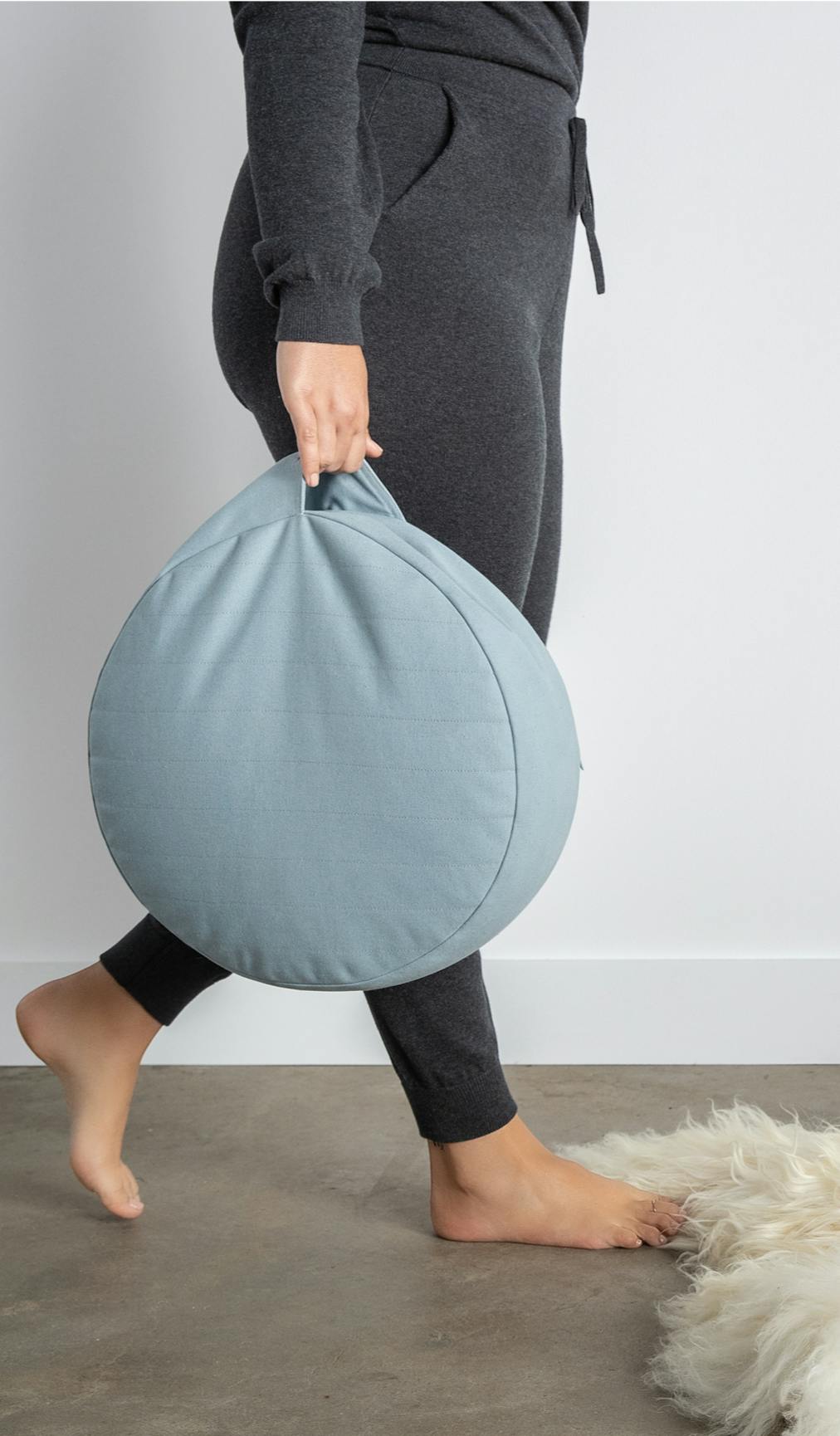 Woman walking with cushion, holding it by the outer pocket.