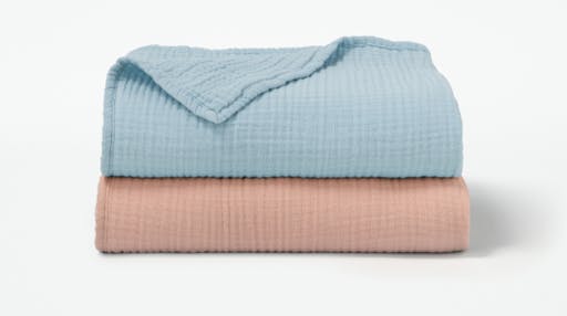 Our Organic Muslin Toddler Blanket in Sea and Blush colors folded and stacked on top of one another