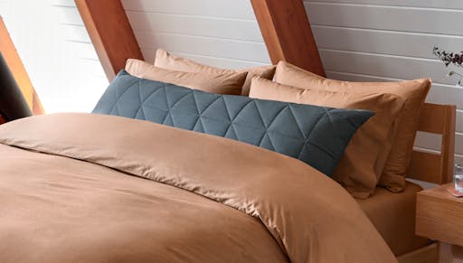 Body pillow with quilted cover on made bed. 