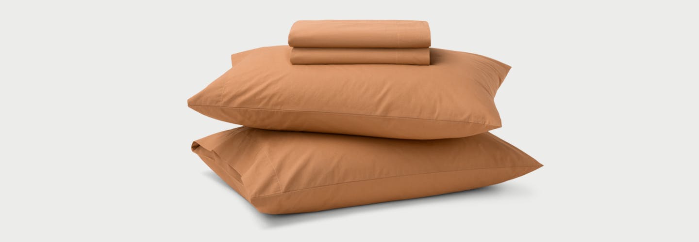 Folded Percale Sheets on top of two pillows in Canyon color.