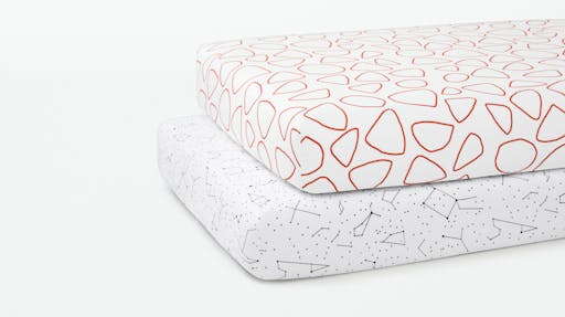 Two crib mattresses stacked on top of one another, fitted with our Pebble and Constellation patterned Crib Sheets