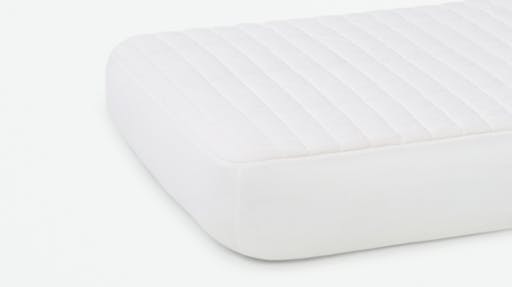 A white Crib Mattress Protector on a crib size mattress laying flat on a white surface