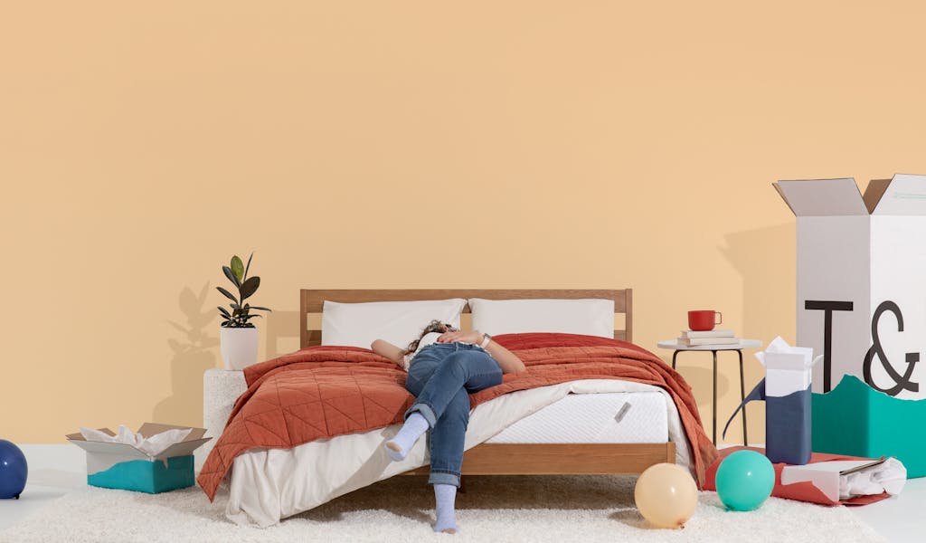 Woman in jeans laying on T&N Original Mattress and Quilt, with balloons on the floor and partially unwrapped birthday gifts.