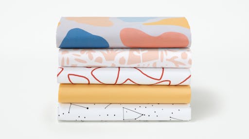 All five Toddler Sheet Set color options (Palette, Flora, Pebble, Sunshine, Constellation) folded and stacked on top of one another