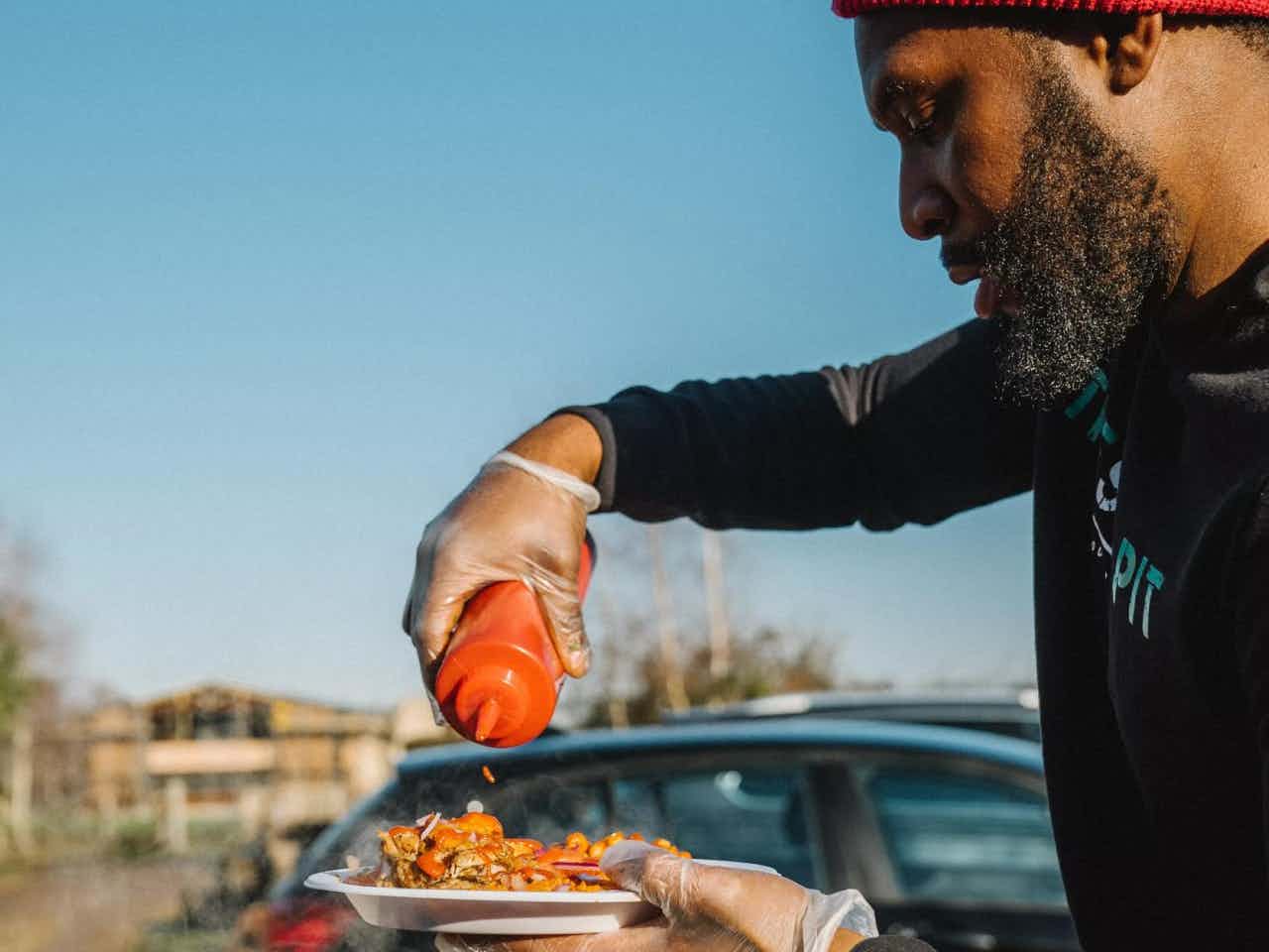 Chef from Suya Pit adds sauce to a street food dish