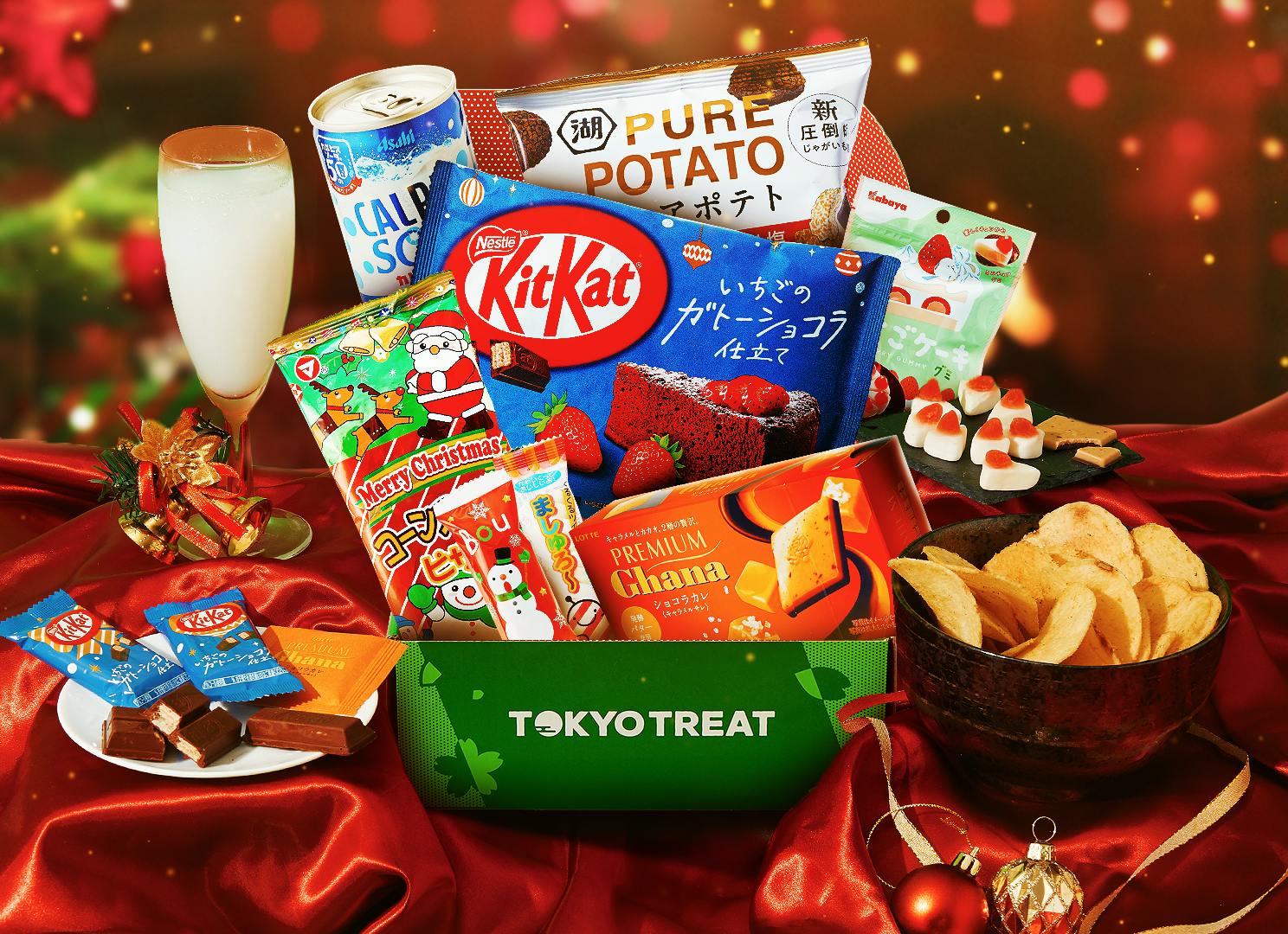 The TokyoTreat Snacktacular Christmas box is sitting on a red satin table, with Christmas lights and other holiday motifs surrounded it. The TokyoTreat Snacktacular Christmas box is sitting on a red satin table, with Christmas lights and other holiday motifs surrounded it.
