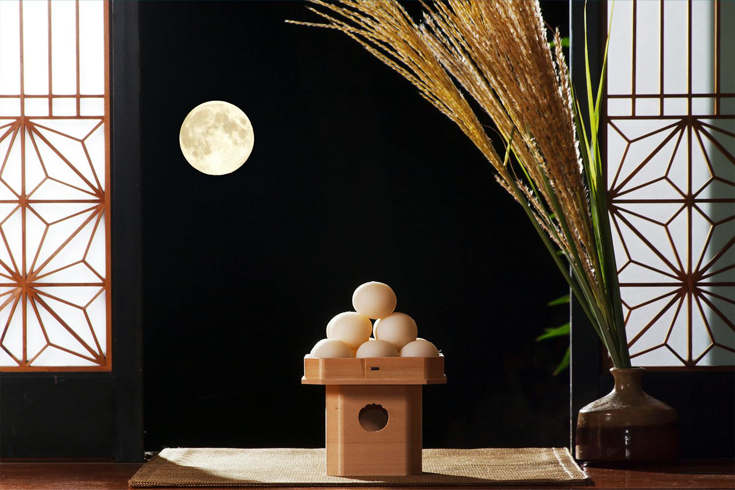 A porch of an old Japanese house is pictured, with Tsukimi elements in the background including: Tsukimi dango, susuki pampas grass, and a glowing harvest moon between two Japanese traditional shoji doors.