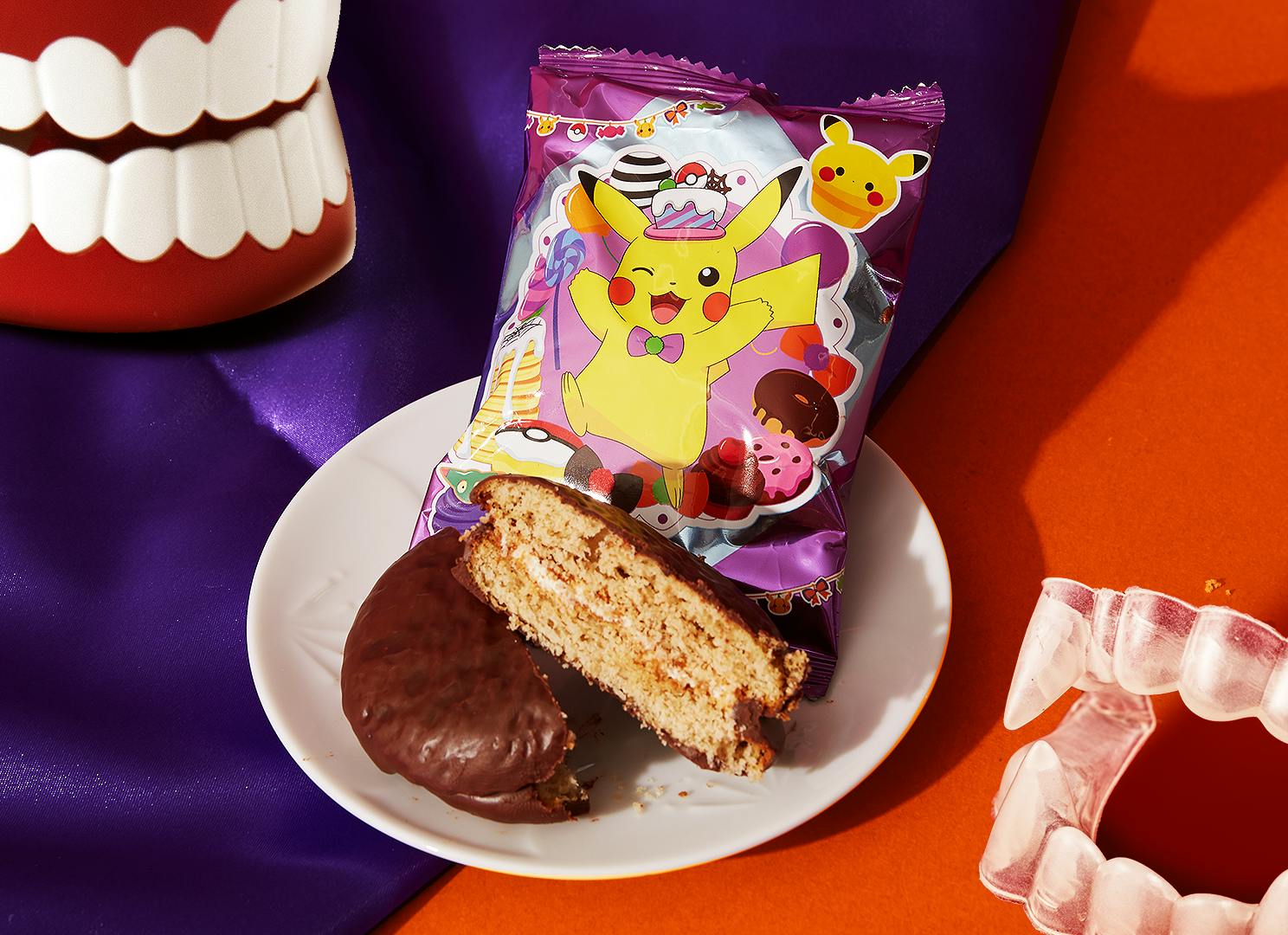 A special Halloween-edition Pokémon Choco Pie sits against a bright red / velvet purple background, next to vampire costume fangs.