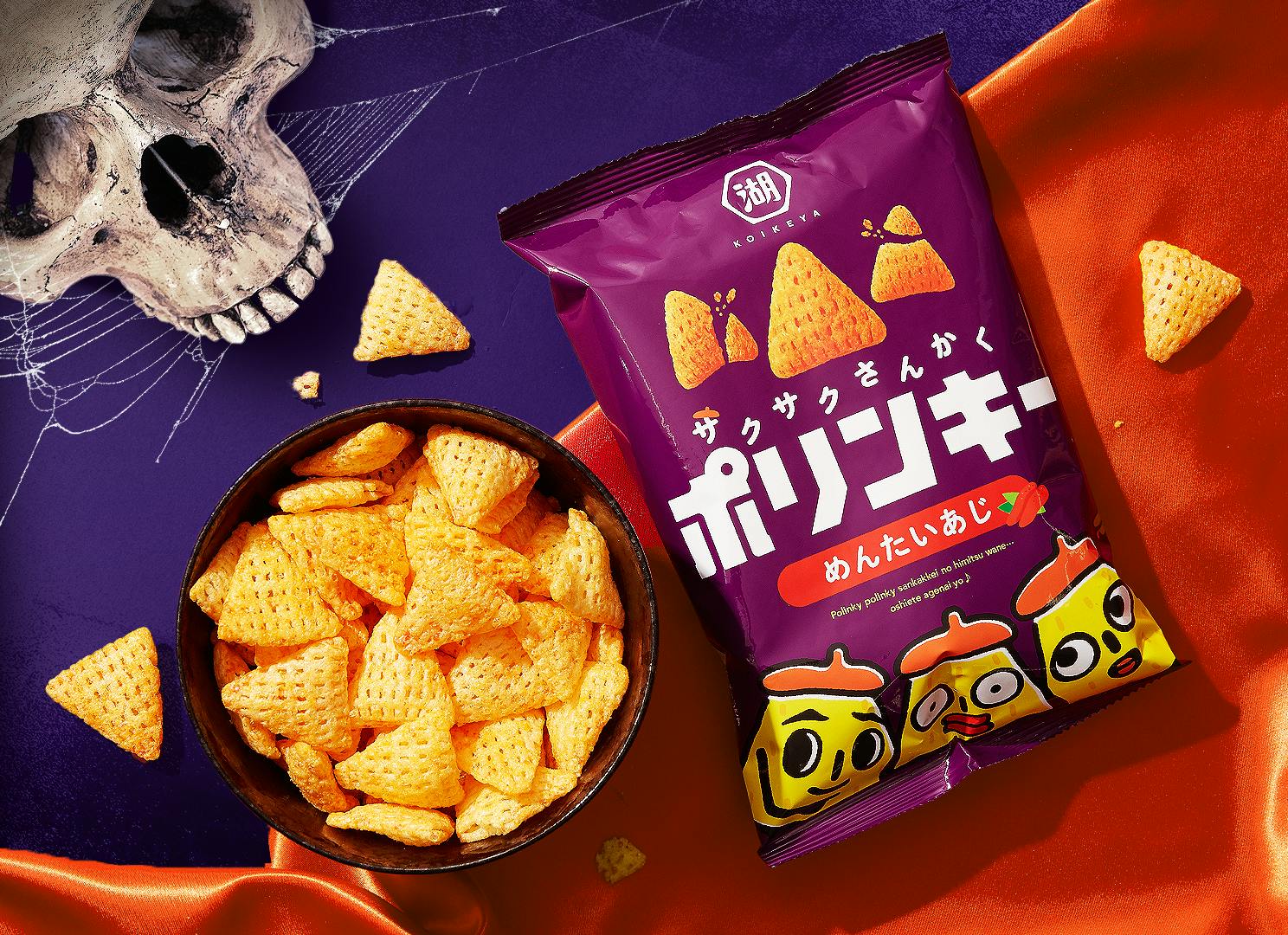 The purple bag of Polinky Mentaiko Corn Snacks sits against a backdrop of red and purple fabric, with a Halloween skull motif nearby.