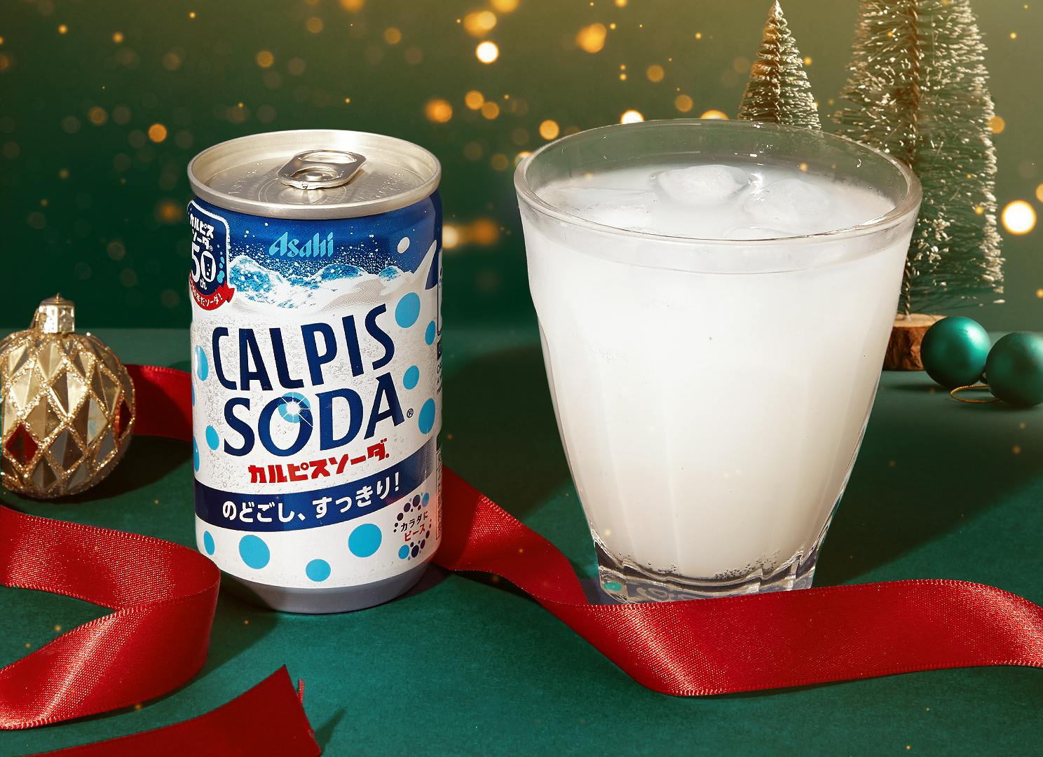 Calpis Soda sits on a table next to Christmas ribbon, small Christmas tree decorations, and golden tree ornaments.